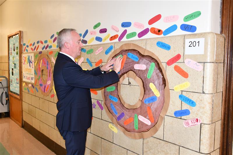 Man in a suit adds a paper sprinkle to a paper donut on the wall